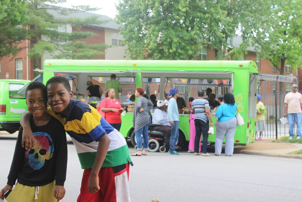 Two children smiling with green bus in the background