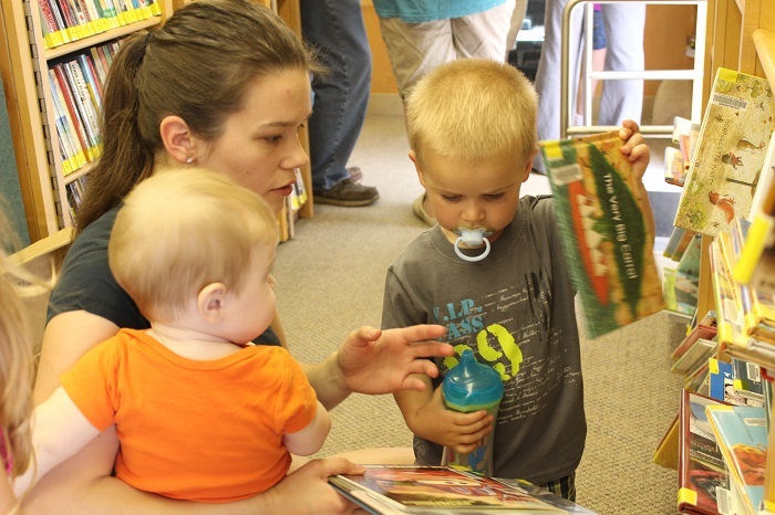 Mother and two children picking out books from a shelf